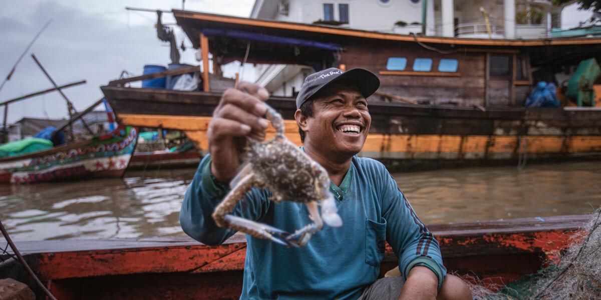 A person smiling as they hold up a crab recently caught on a small fishing boat