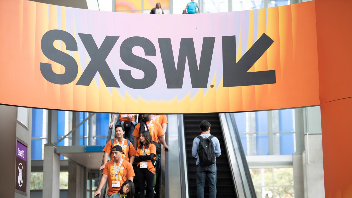 Banner with SXSW logo above conference attendees on escalators