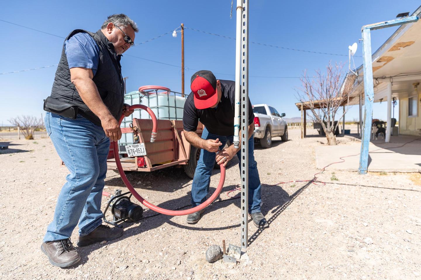 José Acosta and Luis Felipe Lujan with a hose getting ready to fill water tanks in the trailer being pulled by a pickup truck