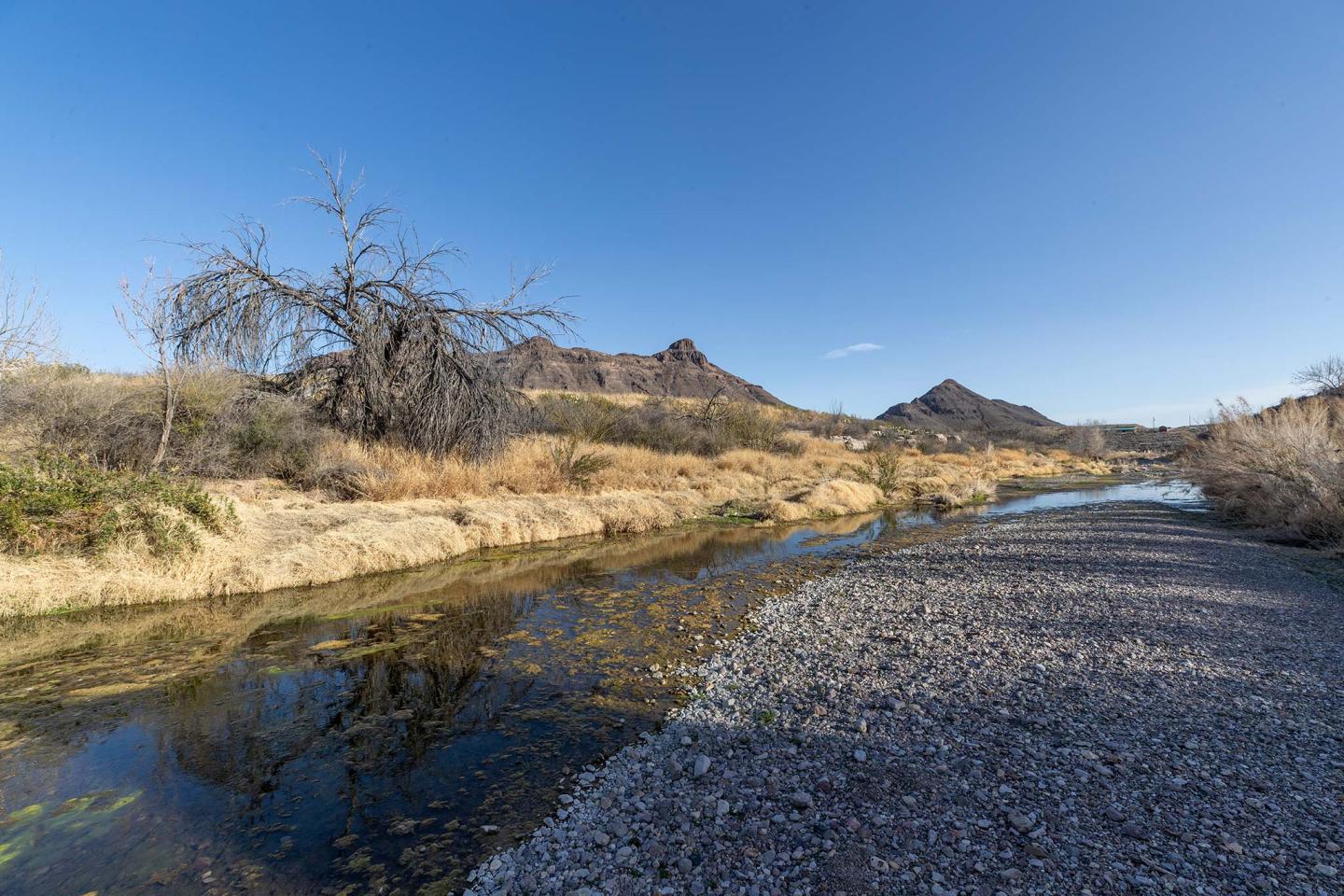 A creek running through desert land with mountains in the background