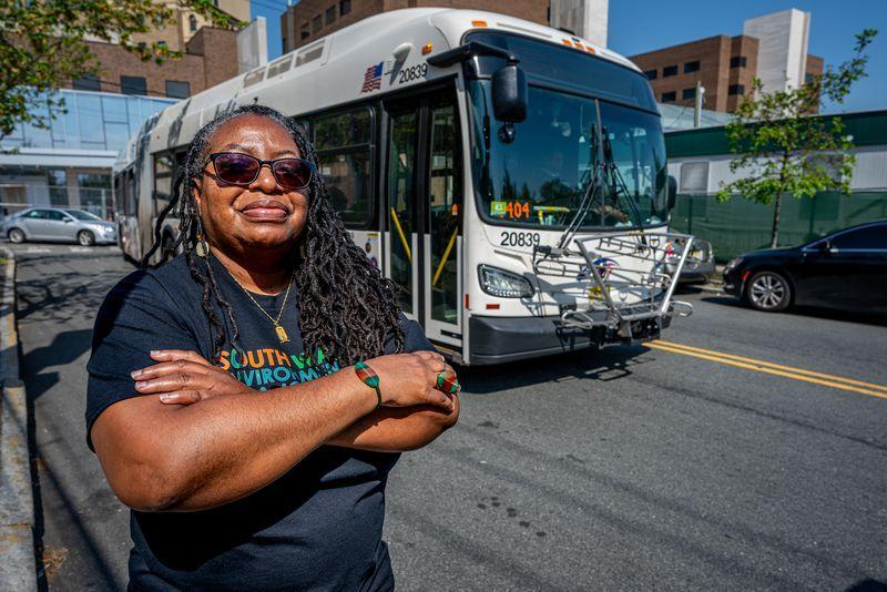 Kim Gaddy standing in front of a road as a bus drives by with her arms crossed