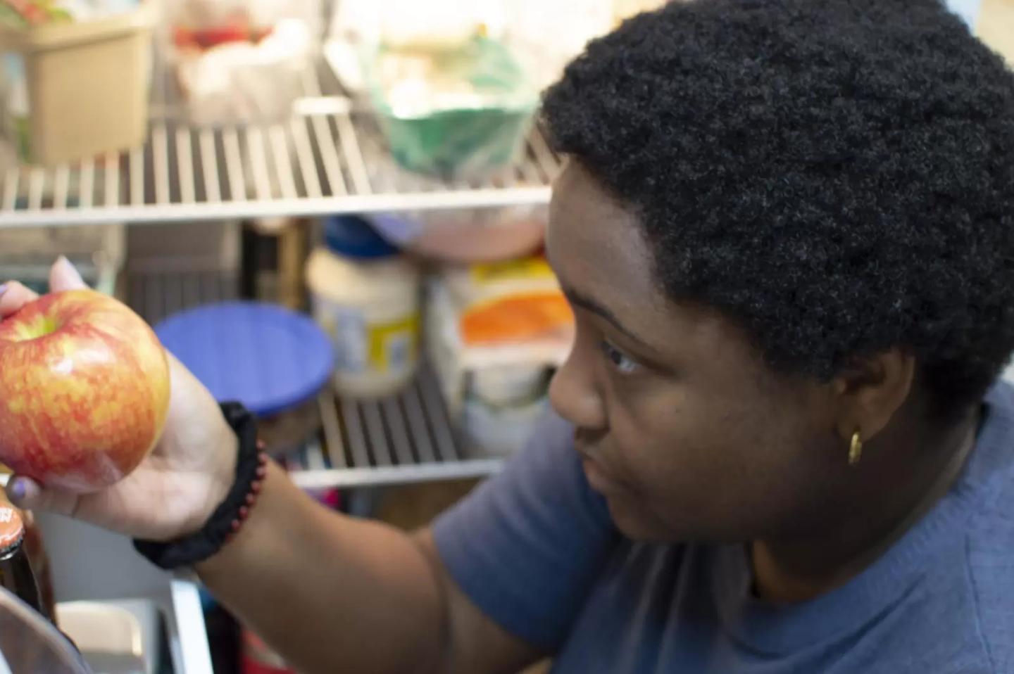 Lee Alisha Williams holding an apple in front of her open fridge