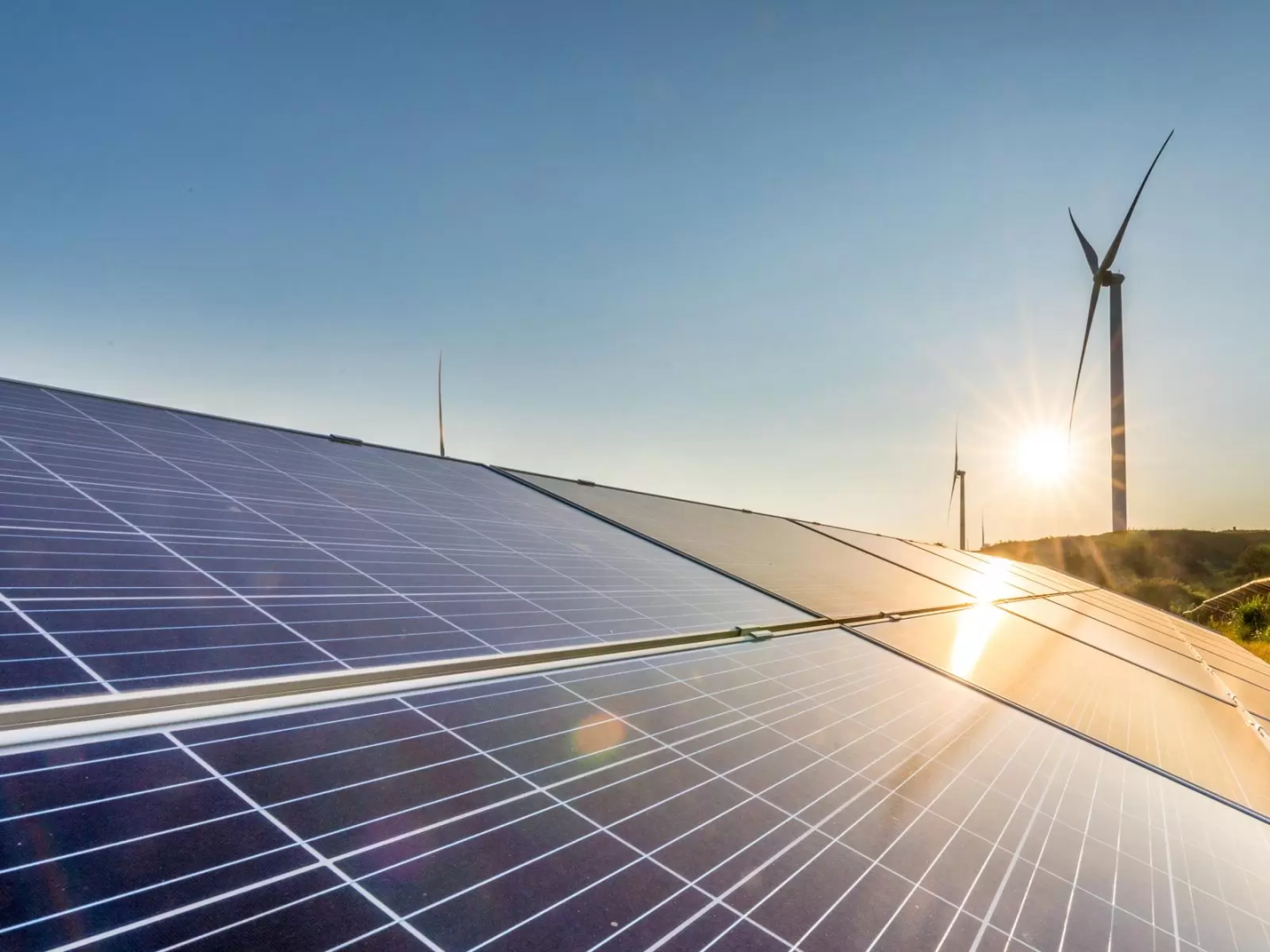 sun glinting off solar panels with a wind turbine in the background