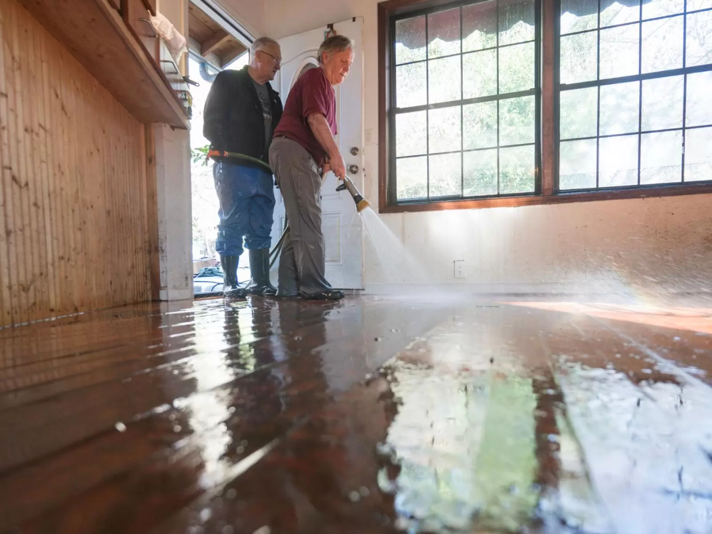 Two people spraying down a the floors of their house with a hose after a flood