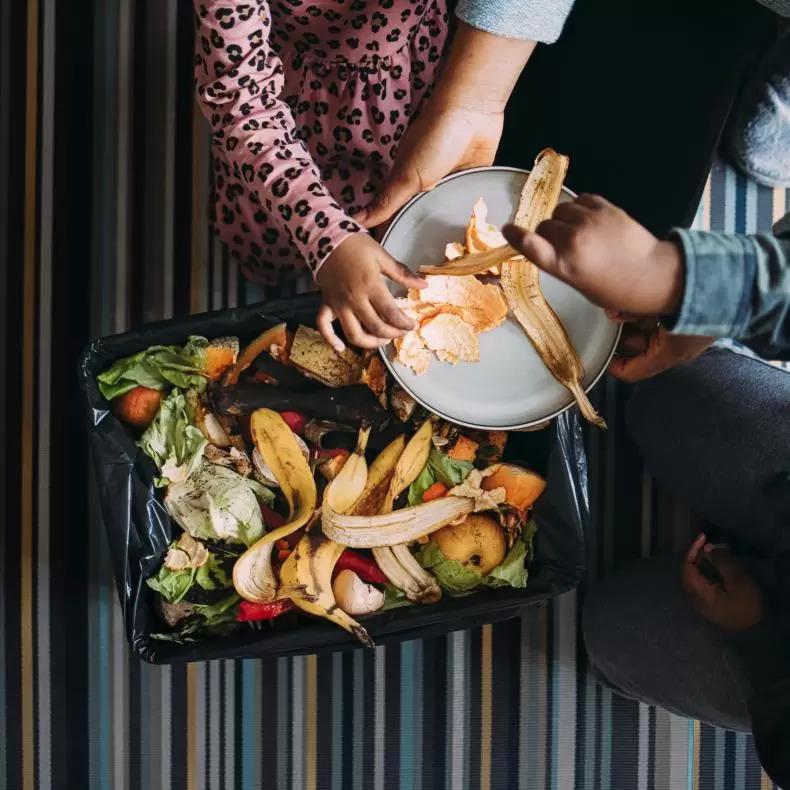 An overhead shot of a family putting fruit peels into a compost bin