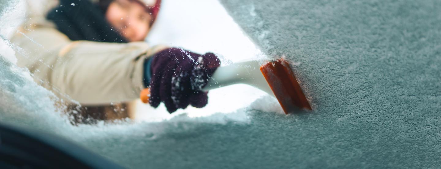 A man scraping snow off a windscreen, shot from inside the car