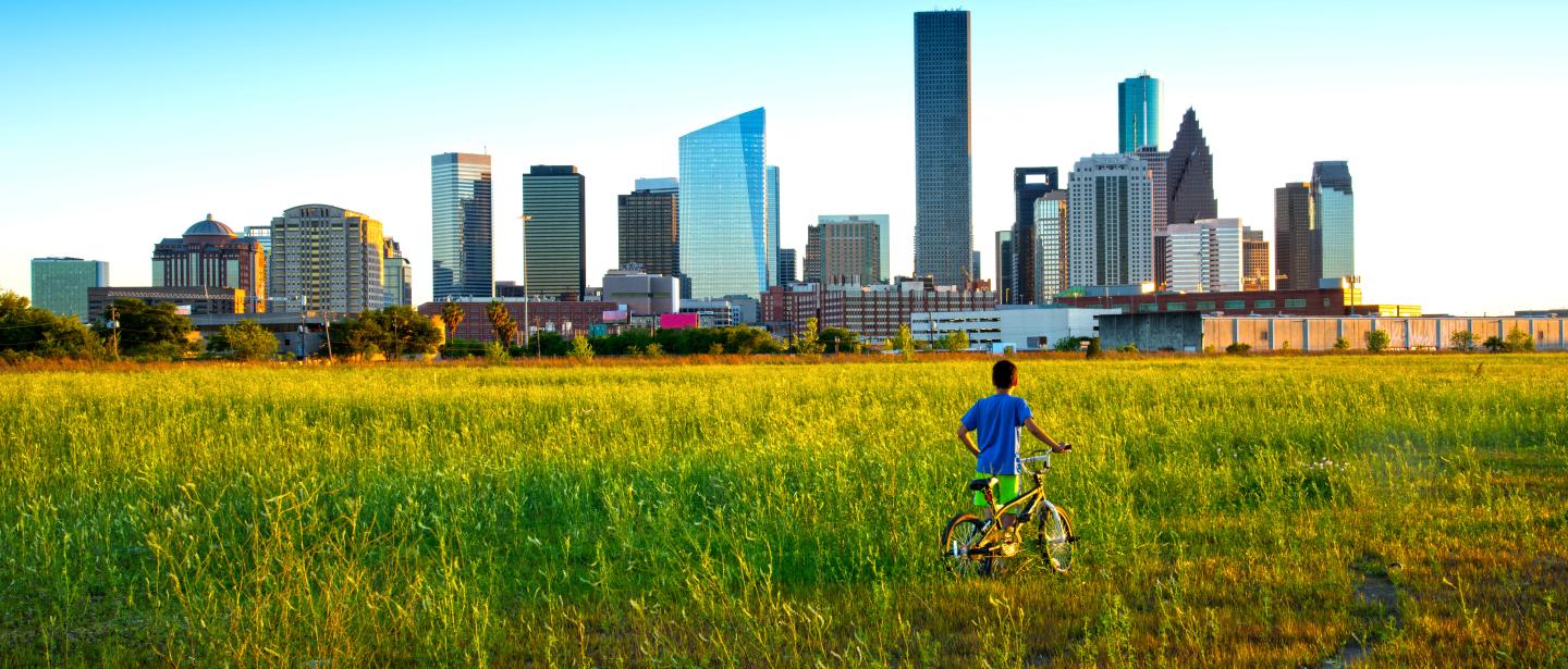 A child pushing a bike in front a city skyline with clear blue skies