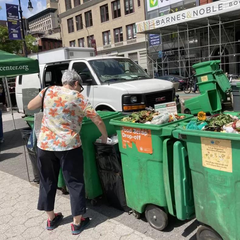 A person putting waste into a row of compost bins