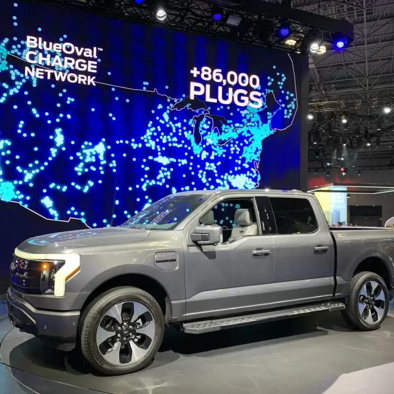 Silver electric pickup truck in front of a digital map display of charging stations nationwide