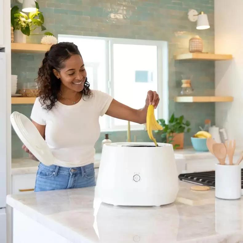 A person putting a banana peel into a countertop composter