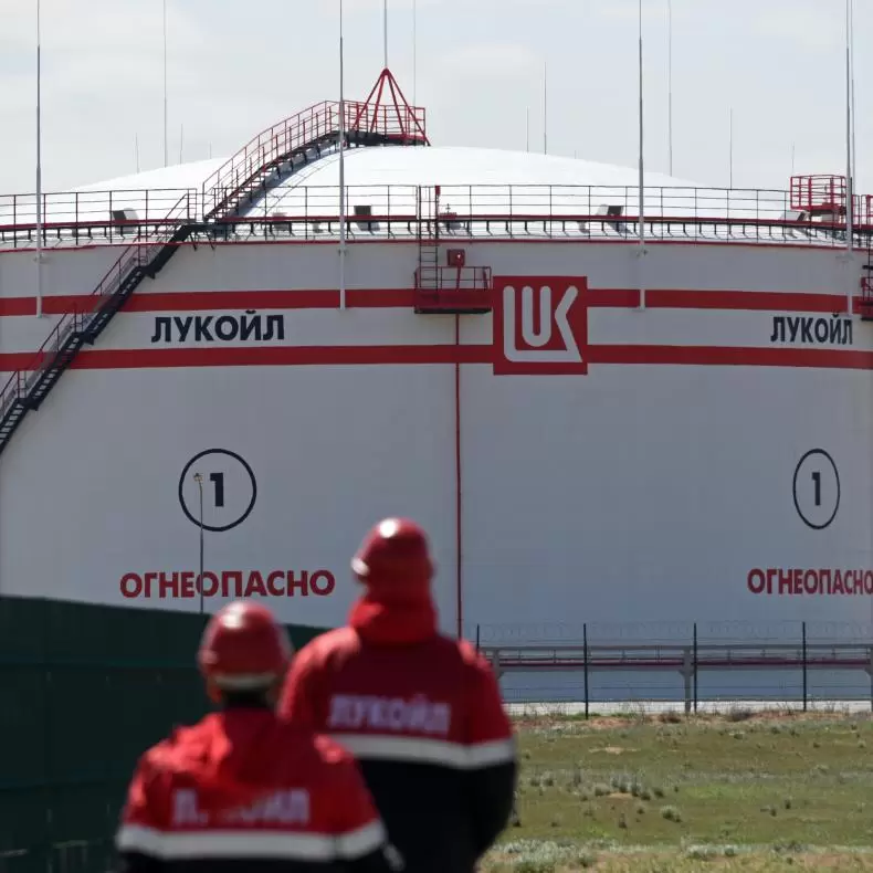 Russian oil and gas workers stand in front of a large storage tank at a refinery.