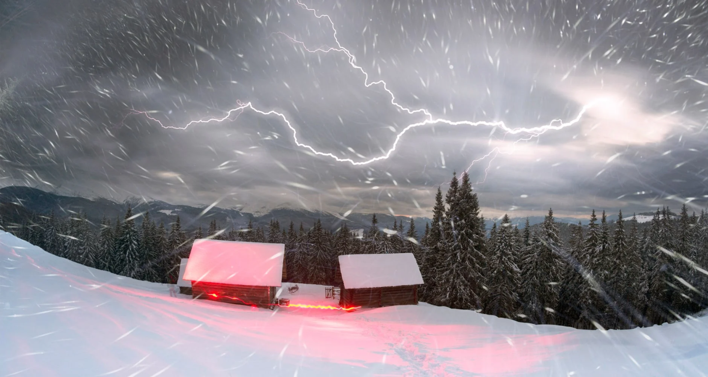 Forked lightning over two snowbound houses, night time scene