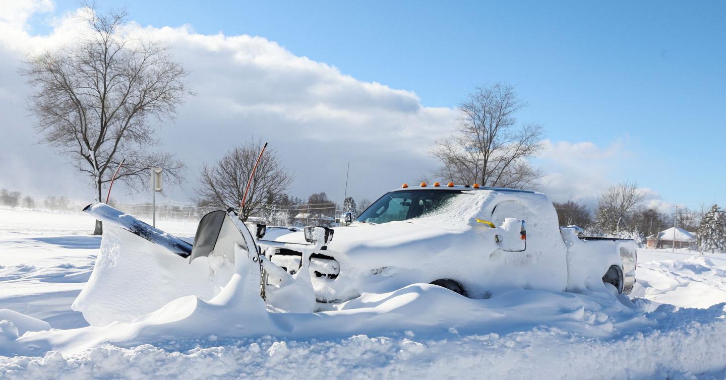 A snow plow buried in snow and stranded on the road following a winter storm 