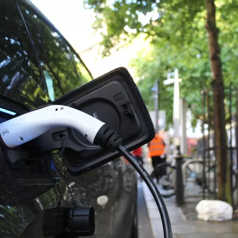 An electric vehicle charging on a tree-lined street