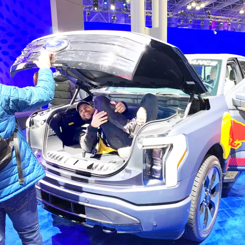 A man gets inside the spacious open "frunk" (front trunk) of an electric truck at an auto show