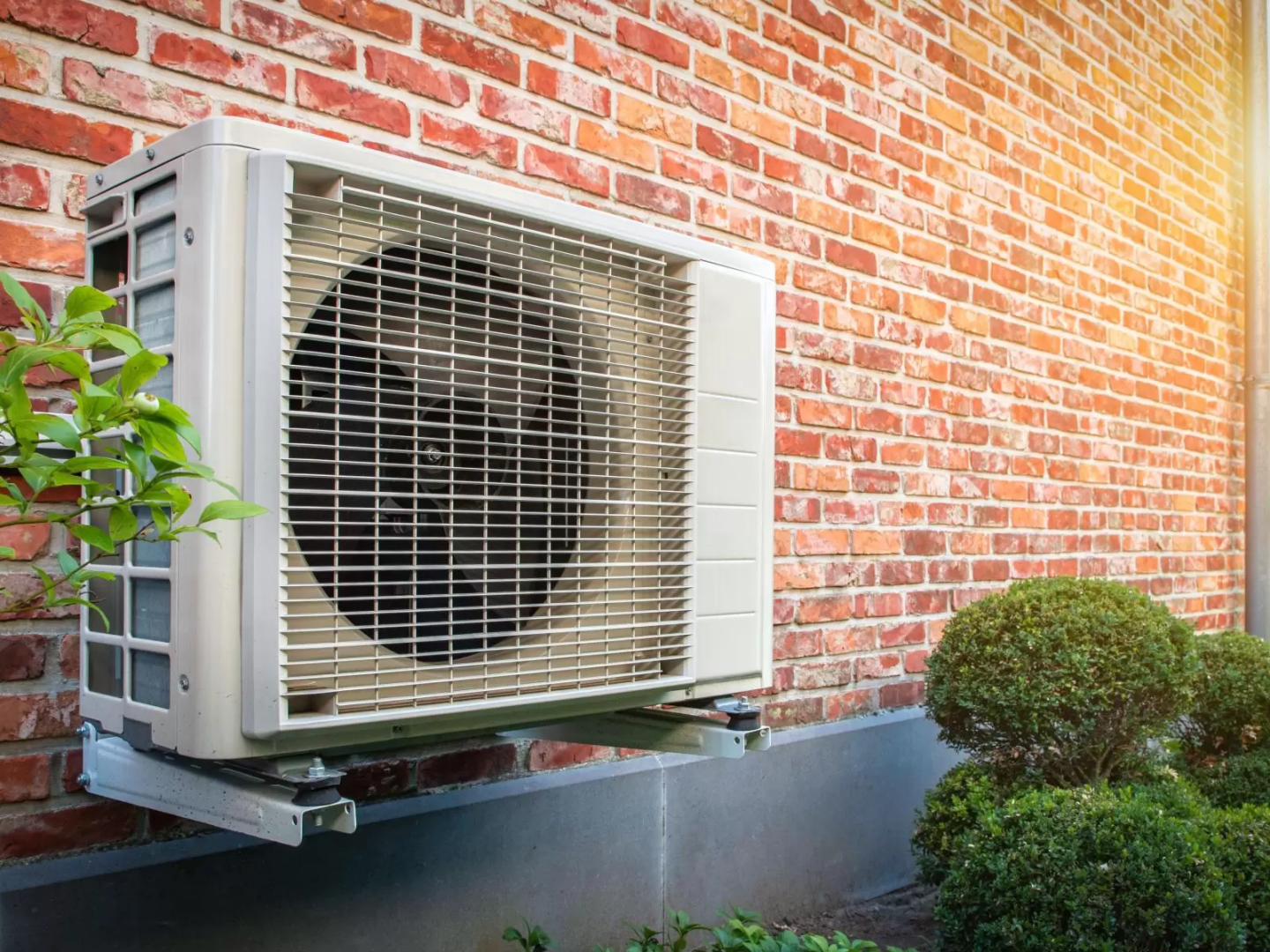 Image of a heat pump outside a brick home. 