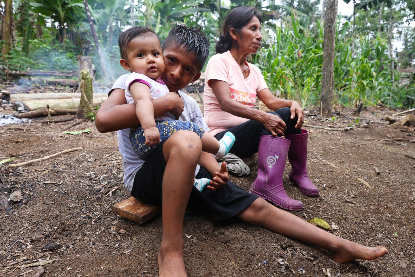 Three members of the Shuar people sitting on a piece of wood