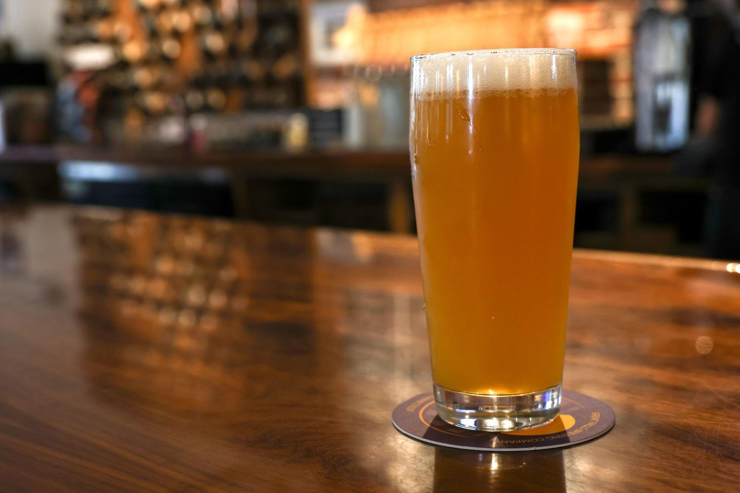 A glass of beer rests on a coaster on a bar top