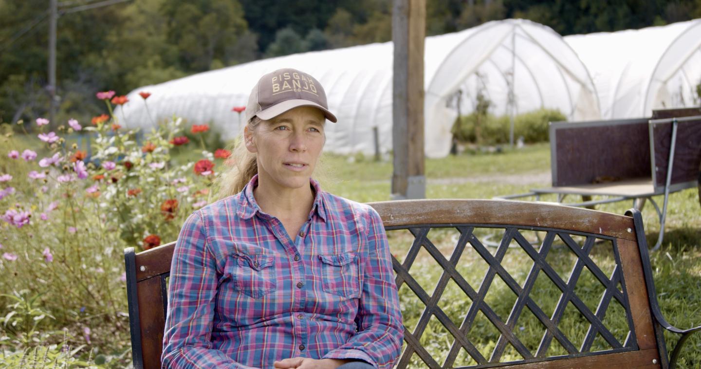 Holly Whitesides of Against the Grain farm sits on a bench in front of growing plants