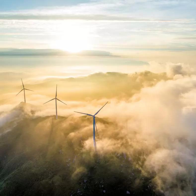 A soaring shot of wind turbines on a mountain ridge with low-lying clouds around them 