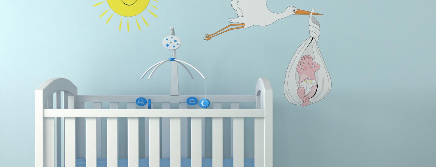 A crib against a blue wall with a sun and a stork carrying a baby