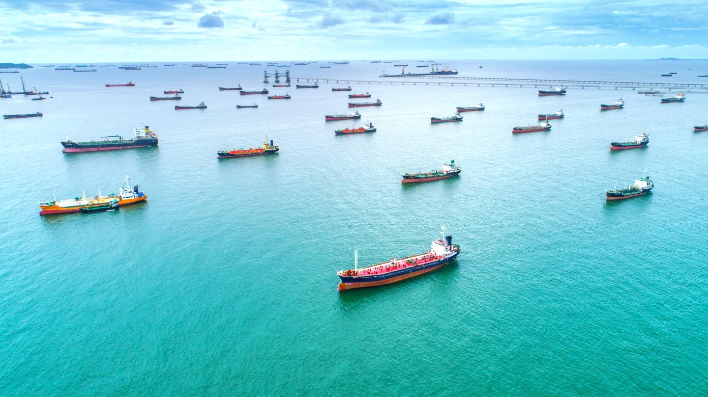 A blue sea dotted with dozens of ships holding shipping containers