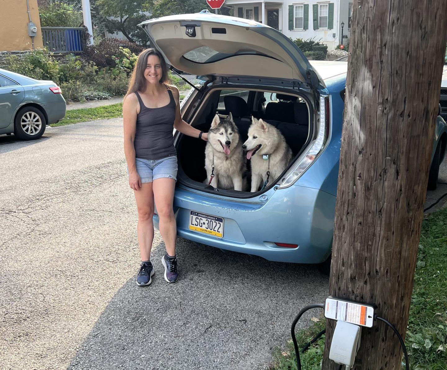 Shana Kennedy standing at the back of her EV with her two large huskies in the hatchback