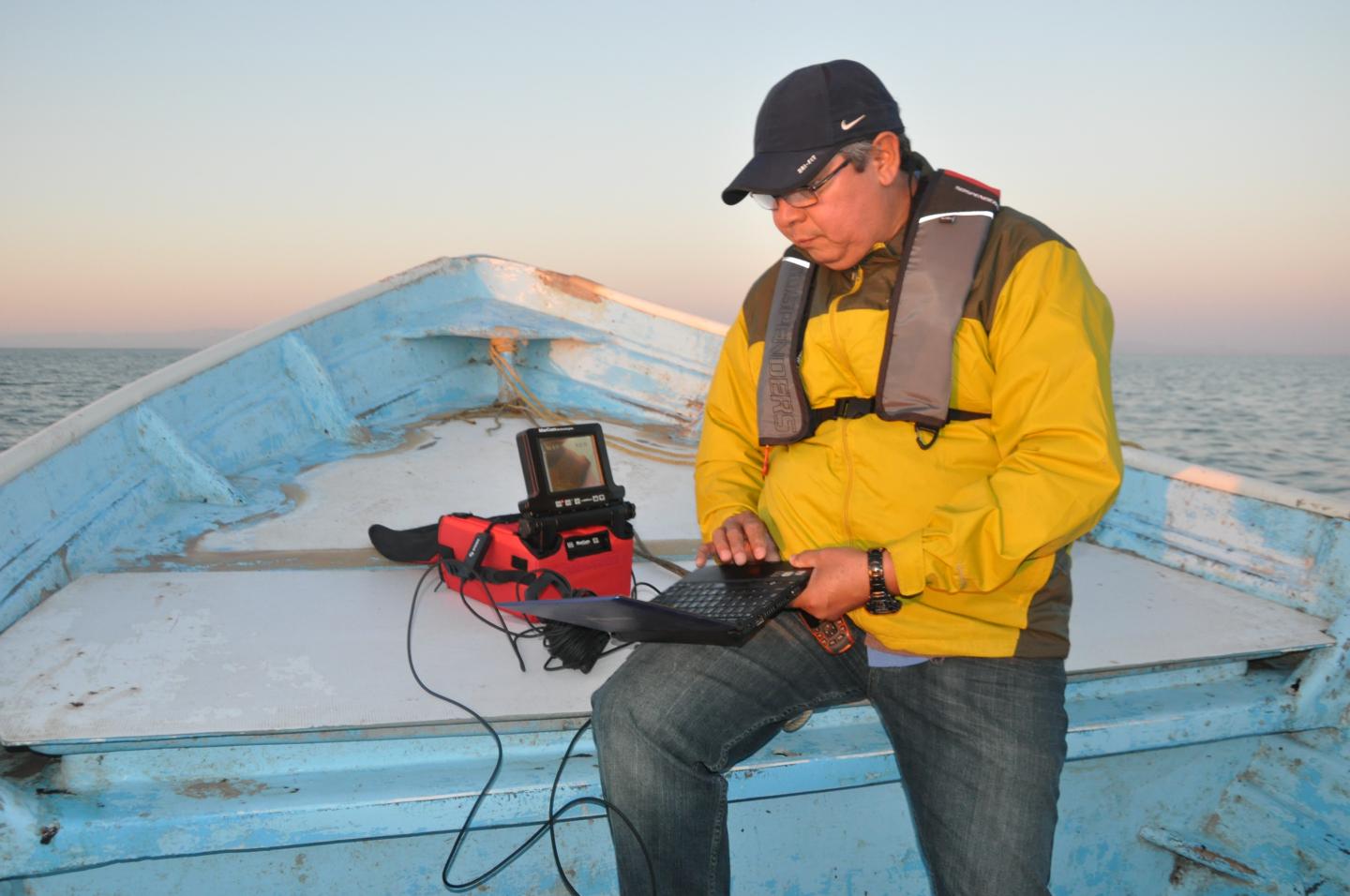 Hector Licon sits on a boat with a laptop 