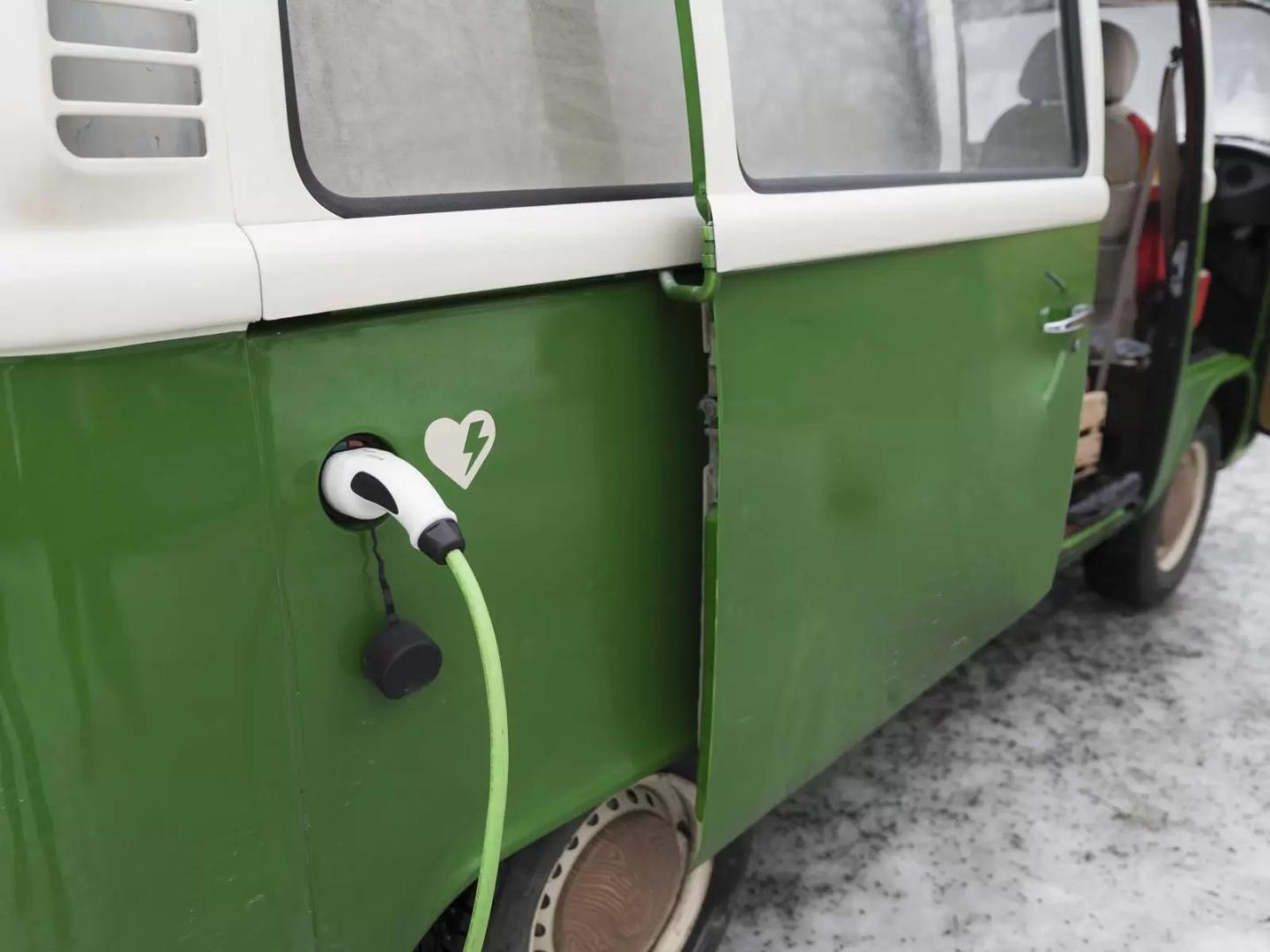 An old van that has been converted into an electric vehicle with a charging cable connected