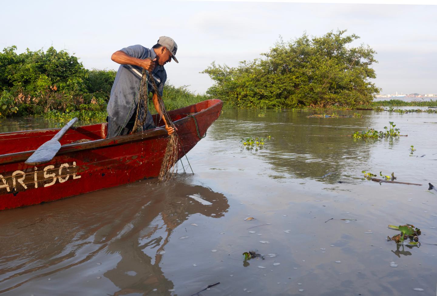 A fisher in a red boat casts a net into the water