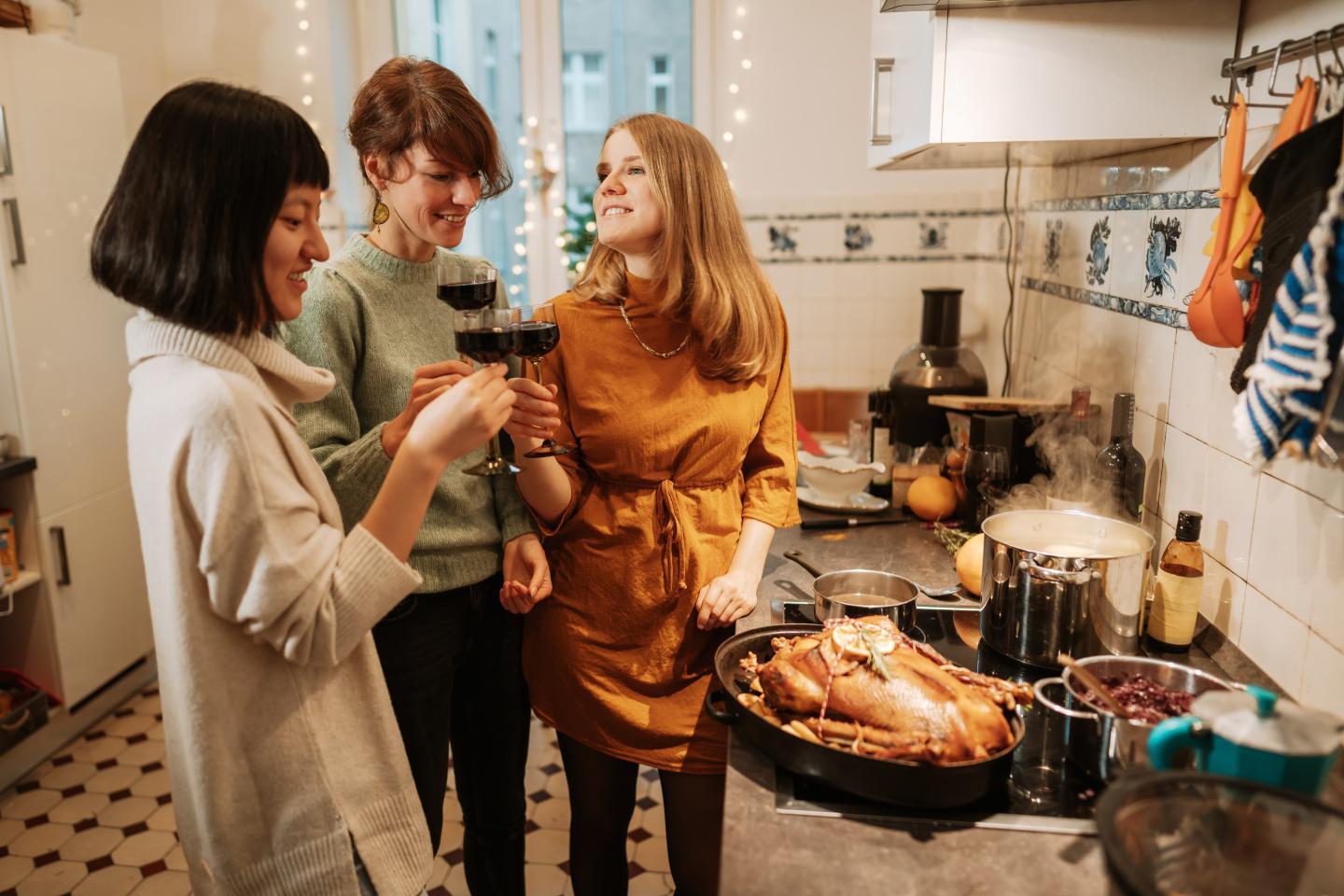 Three people with glasses of wine standing next to a cooked turkey