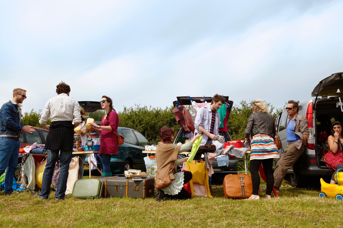 A row of people selling belongings out of the trunks of their cars