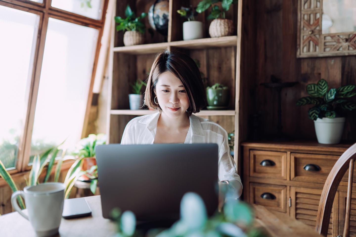 A person sitting at a table working on a computer with many plants around them 