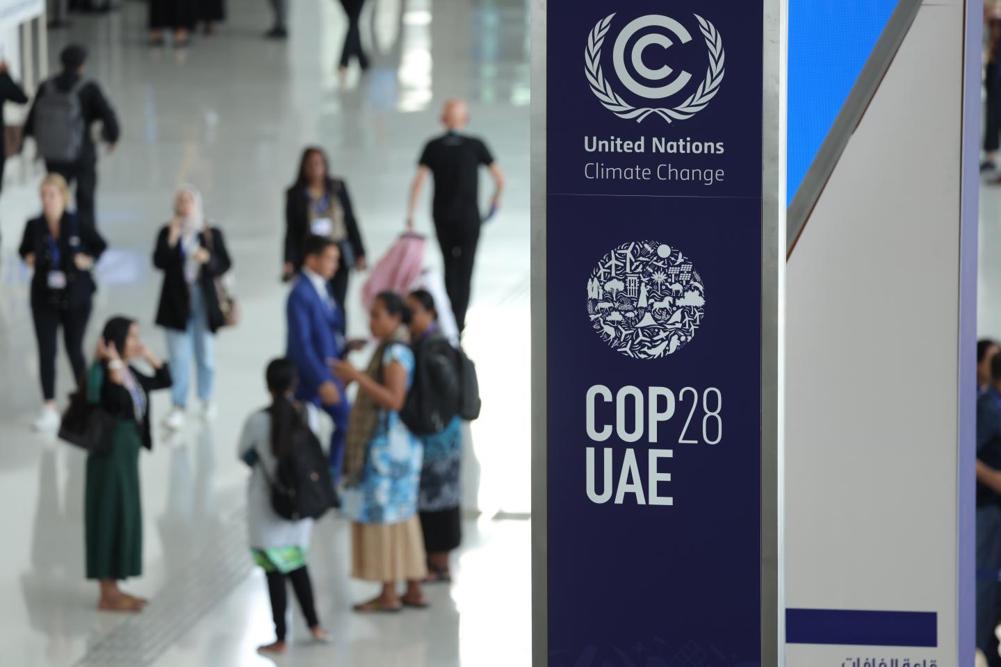 A COP28 sign in the foreground with people gathered in the background