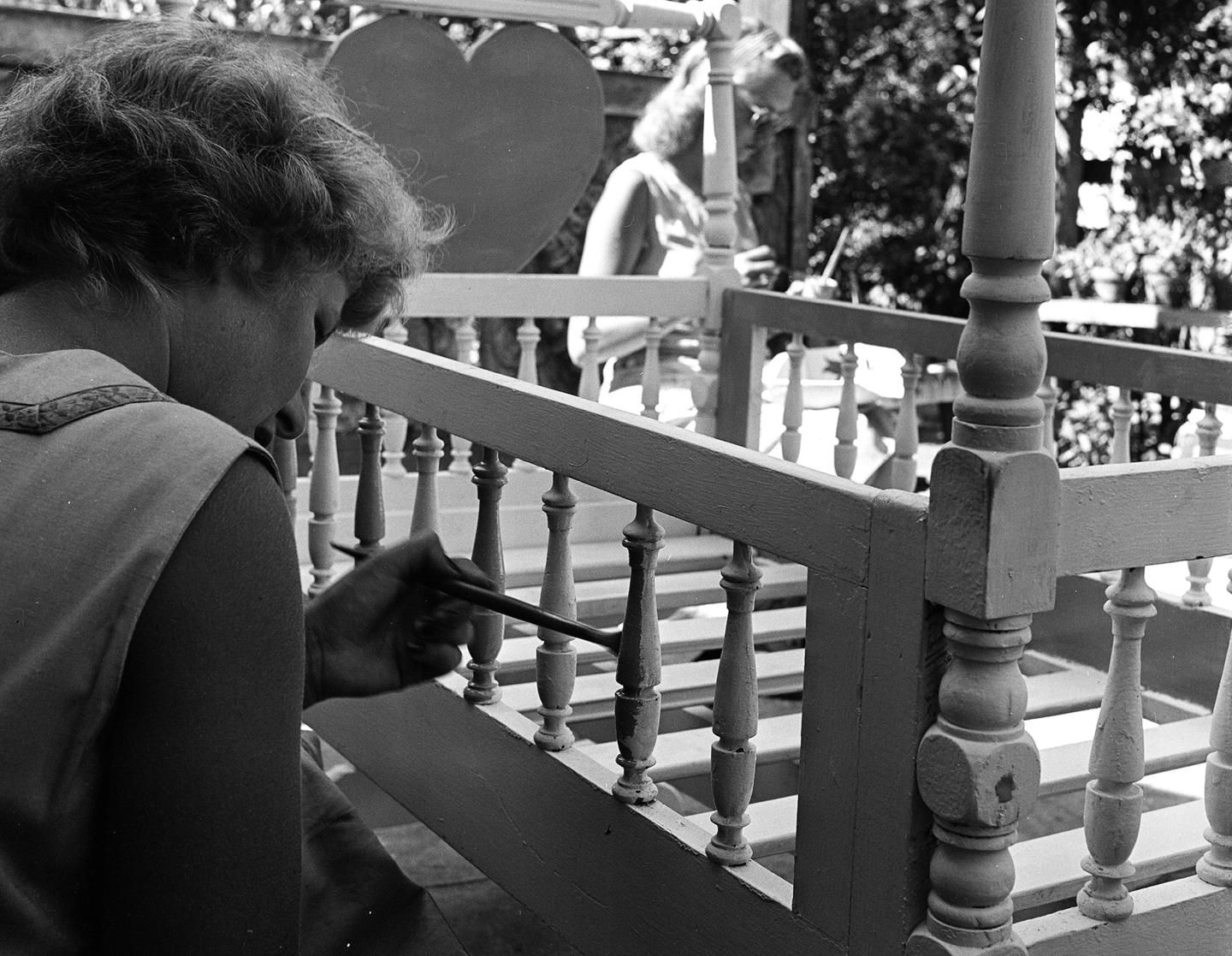 A black and white photo of a woman painting a crib in the 1940s