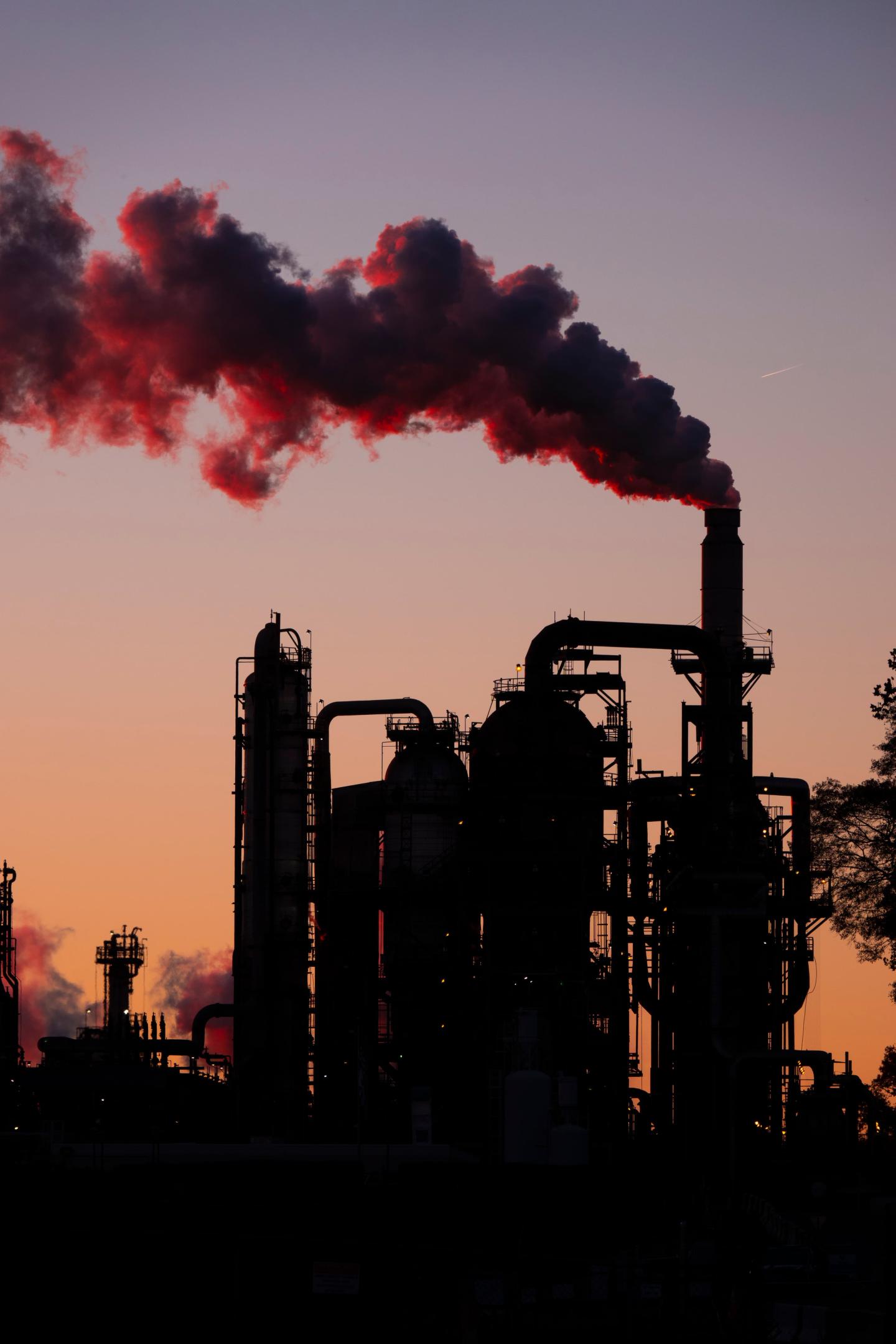 A power plant at sunset with billowing smoke coming out of it