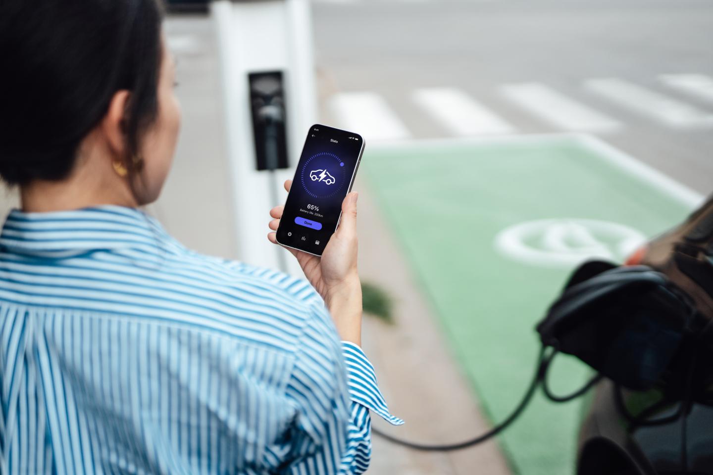 A person checks a smart phone app to see how long their EV has left to charge