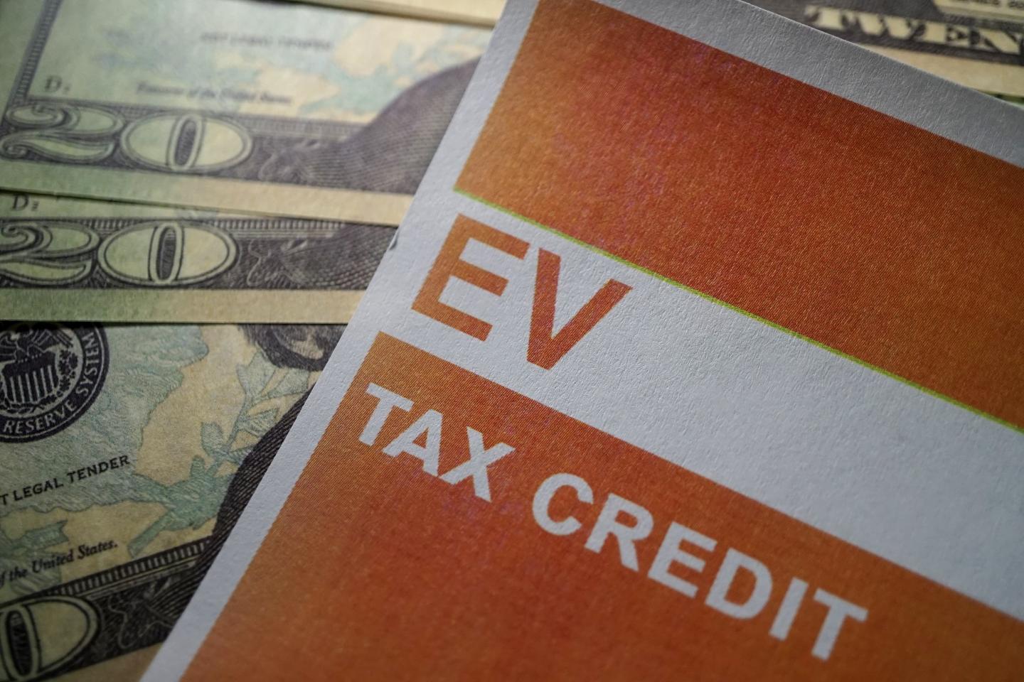 A pamphlet with EV tax credit written on it and cash behind it