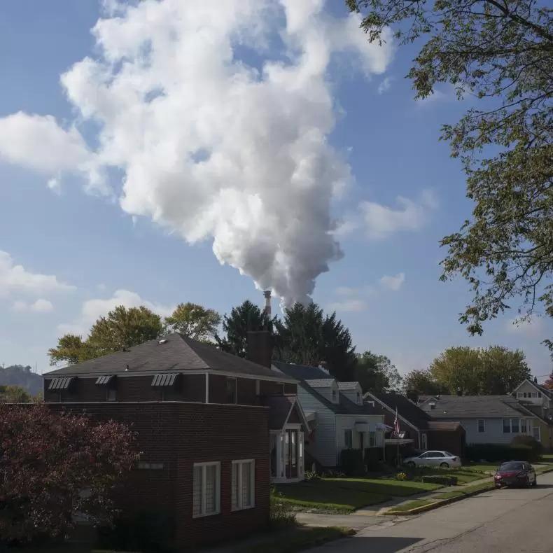 A row of suburban homes with a power plant spewing plumes of smoke directly in the background