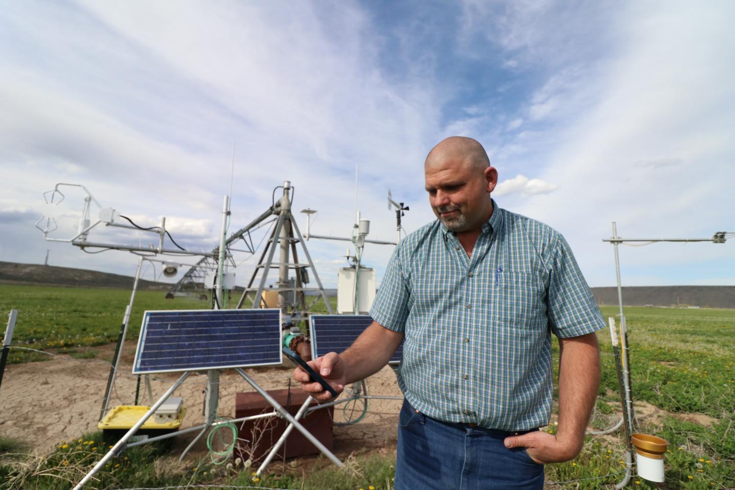 Farmer Mark Owens uses OpenET on a device with more technological equipment in the background