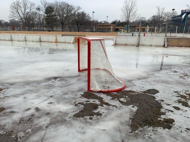 A hockey net on an outdoor rink with mud around it from the ice melting