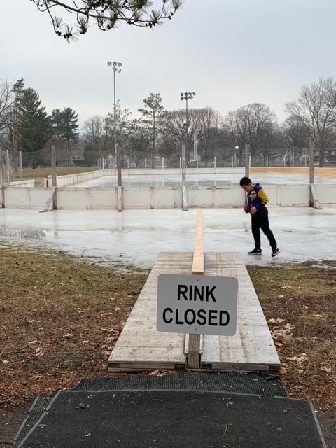 A sign that reads "rink closed" with an outdoor ice rink melting in the background