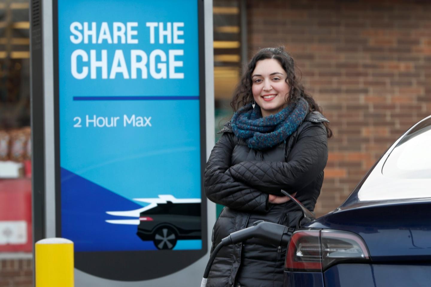 Neda Deylami stands in front of a sign that reads "share the charge"