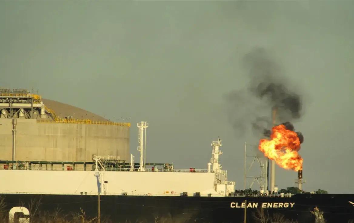 A large ship marked "clean energy" ironically in front of a natural gas flare
