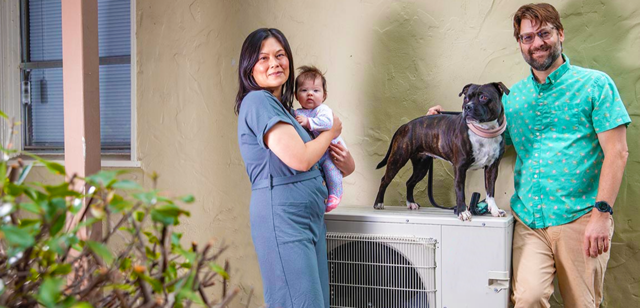 The Grow family standing next to their heat pump with their dog on top of it