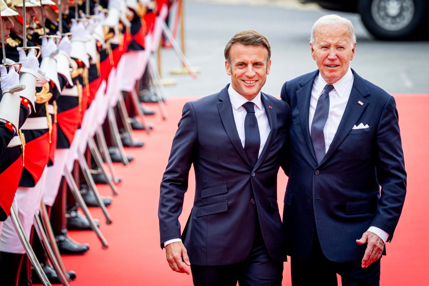 Presidents Emmanuel Macron and Joe Biden walking on a red carpet commemorating D-Day