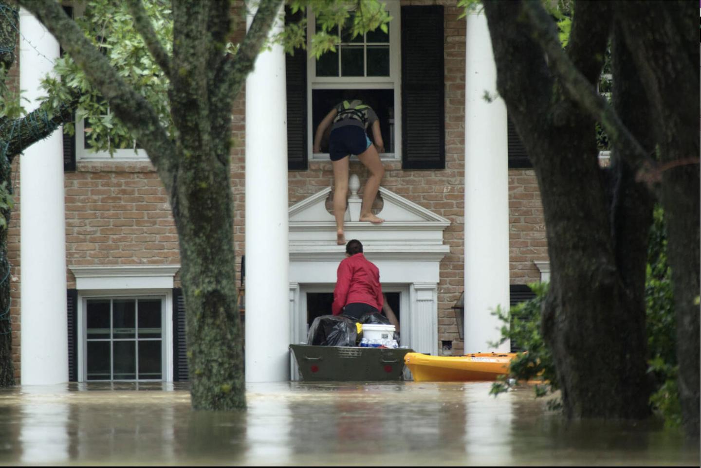 A person climbing out of a second story window into a boat as flood waters block the first level