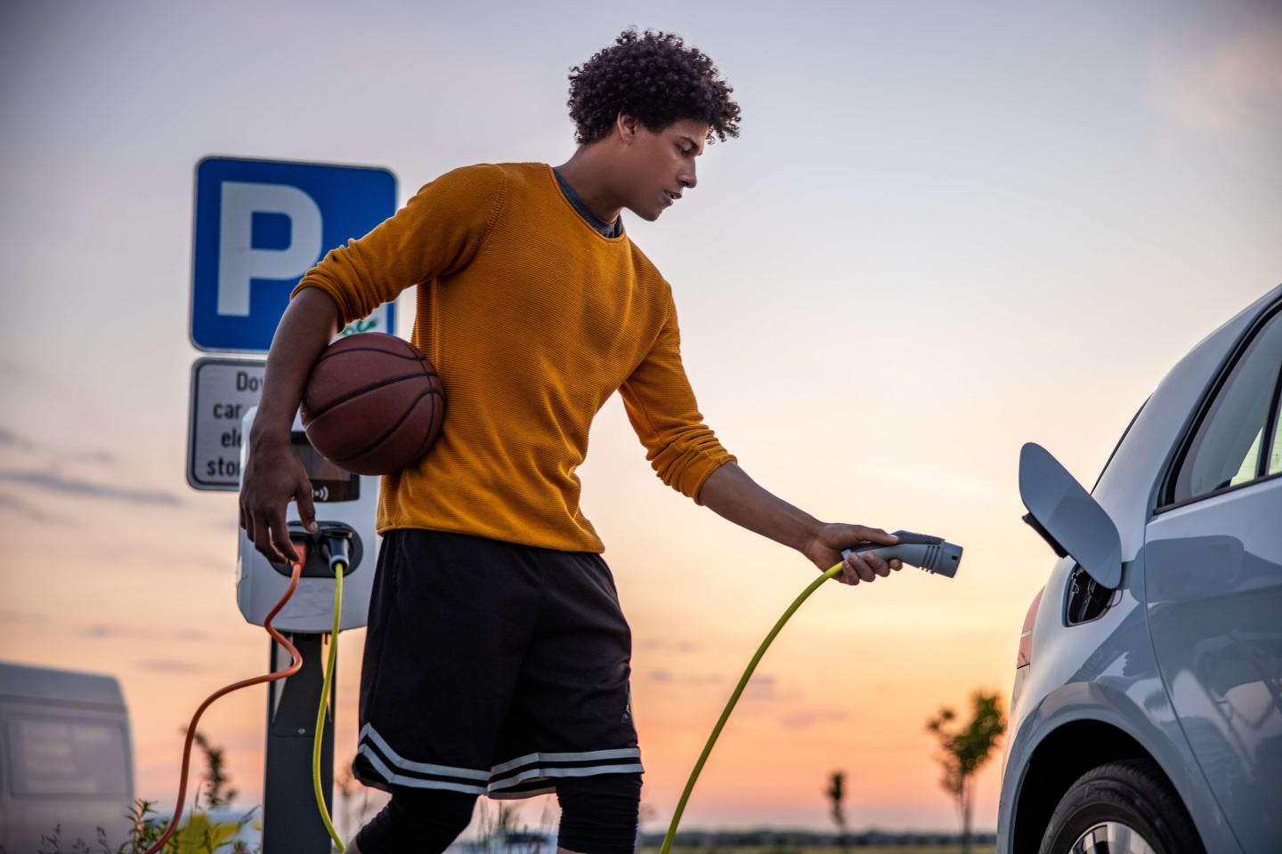 Someone plugging their electric car in while holding a basketball