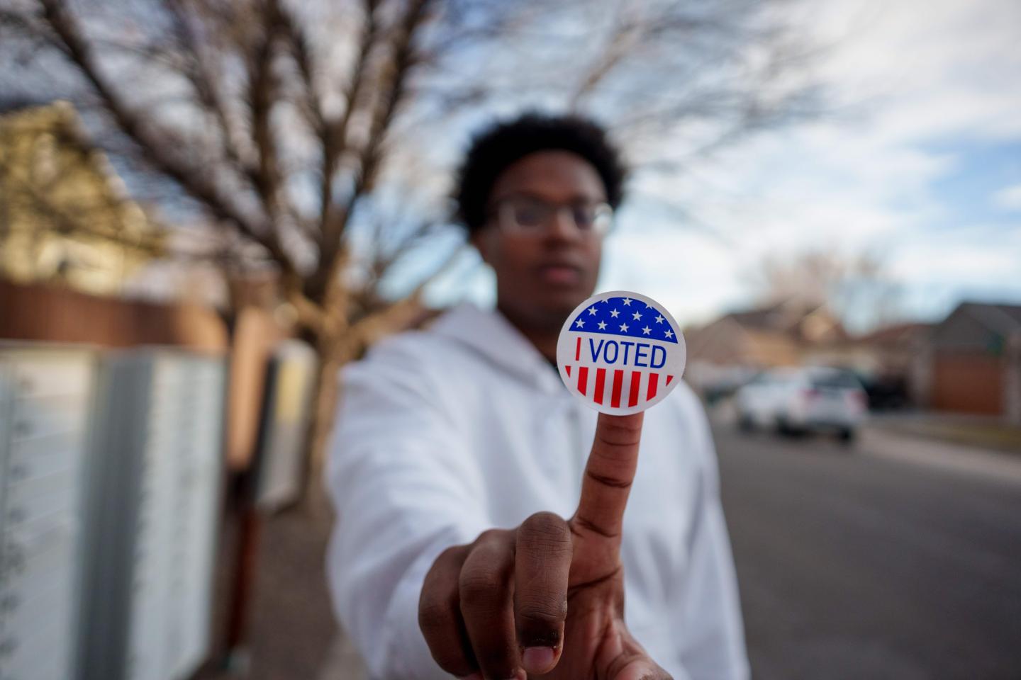 A person holding up an "I voted" sticker stuck to their finger