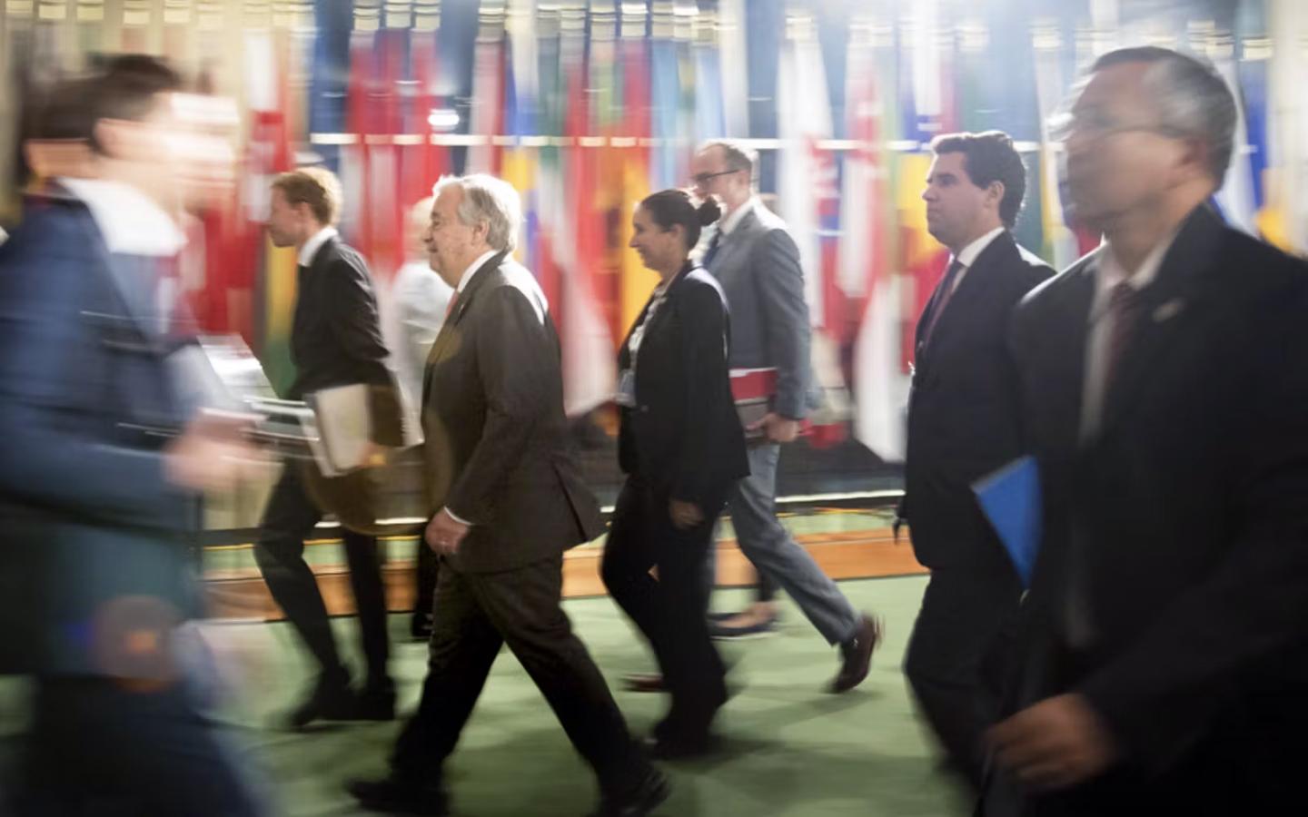 A group of people moving with such speed that some of them are blurry in front of a row of flags at the United Nations